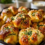 A cast iron pan filled Garlic Knots Recipe with golden, buttery garlic knots topped with parsley.