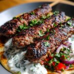 Grilled Lebanese kafta skewers served on flatbread with tzatziki, diced tomatoes, red onions, and fresh herbs. Charred meat and creamy sauce create a bold contrast.