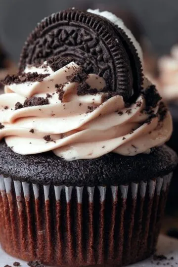 A Oreo Cupcake Recipe topped with swirls of Oreo-speckled frosting, half an Oreo cookie, and cookie crumbs.