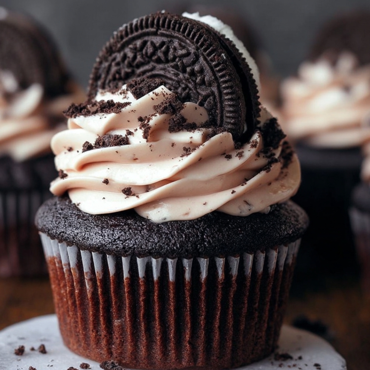 A Oreo Cupcake Recipe topped with swirls of Oreo-speckled frosting, half an Oreo cookie, and cookie crumbs.