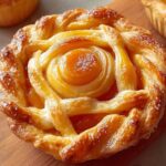Mini peach pie tart with golden lattice crust styled like a rose, placed on a wooden board with glossy finish and sugar crystals.