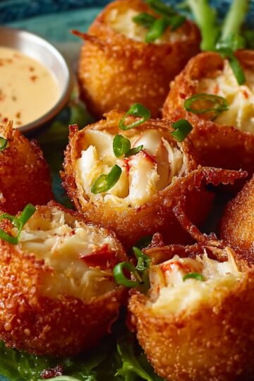 Fried Rangoon Crab Bombs on a plate with greens, served with a dipping sauce, garnished with green onions.