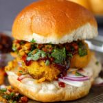 A vibrant street-food scene with vendors serving hot vada pav recipe sandwiches.