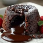 Rich chocolate lava cake recipe on a white plate with molten chocolate oozing from the center, garnished with fresh strawberries, chocolate chips, and a dusting of powdered sugar.