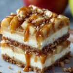 A close-up of a decadent caramel apple cheesecake bars, layered with crust, cheesecake, apple filling, and dripping caramel sauce on top.
