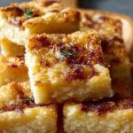 Caramelized Parmesan Onion Squares and cheese squares stacked on a wooden platter, golden and crispy on top with herbs sprinkled for garnish.