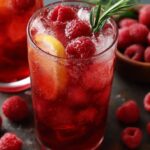 Two tall glasses of raspberry iced tea with lemon slices, raspberries, ice, and a rosemary garnish.