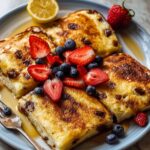 A plate of baked Sheet Pan Pancakes squares topped with fresh strawberries, blueberries, syrup, and a lemon wedge.