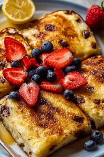 A plate of baked Sheet Pan Pancakes squares topped with fresh strawberries, blueberries, syrup, and a lemon wedge.