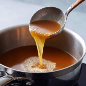 Apple cider reduction being ladled from a saucepan during cooking.