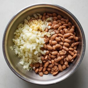 Metal bowl with cooked beans, chopped onions, and minced garlic
