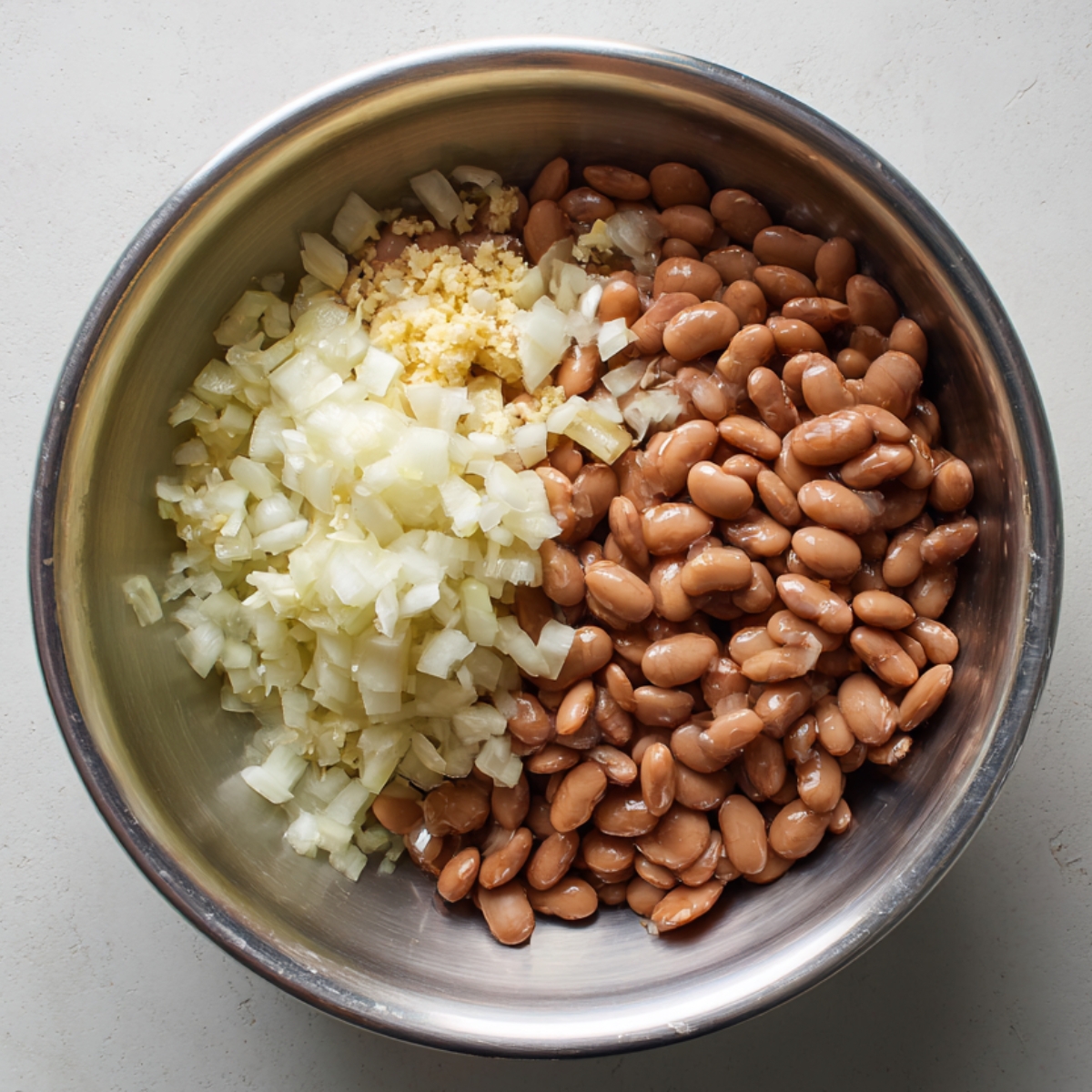 Metal bowl with cooked beans, chopped onions, and minced garlic