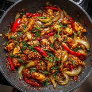 Black pepper chicken stir-fry in a hot wok with red bell peppers, onions, scallions, and sesame seeds in a glossy, spicy sauce