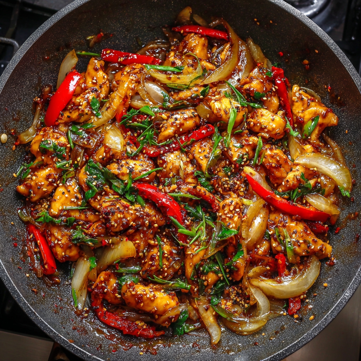 Black pepper chicken stir-fry in a hot wok with red bell peppers, onions, scallions, and sesame seeds in a glossy, spicy sauce
