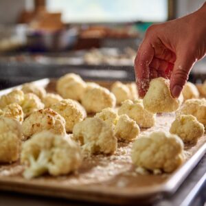 Person chopping fresh cauliflower florets on a cutting board with butter in the background.