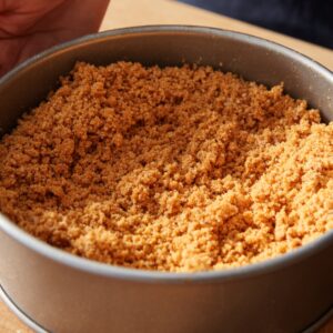 A baking pan filled with pressed graham cracker crust, smoothed with a spoon.