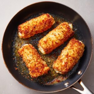 Golden-brown chicken cordon bleu rolls are sizzling in a frying pan with bubbling oil and seasoning.