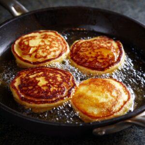 Four golden pancakes cooking in a skillet over medium heat.