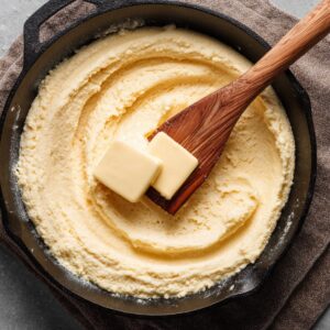 Unbaked cornbread batter spread evenly in a cast iron skillet with cubes of butter melting on top, ready to go into the oven.