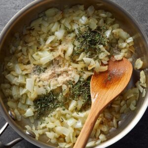 Chopped onions sautéing in a pan with fresh thyme and seasonings.