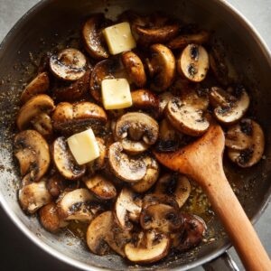 Sliced mushrooms cooking in butter and black pepper in a skillet.