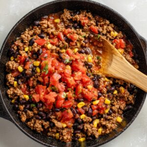 A skillet filled with ground beef, diced tomatoes, black beans, and corn, simmering together.