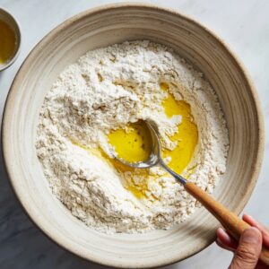 A large bowl with flour and olive oil in the center, with a wooden spoon.