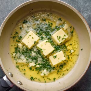 Cubes of butter melting with minced garlic and chopped parsley in a small skillet.