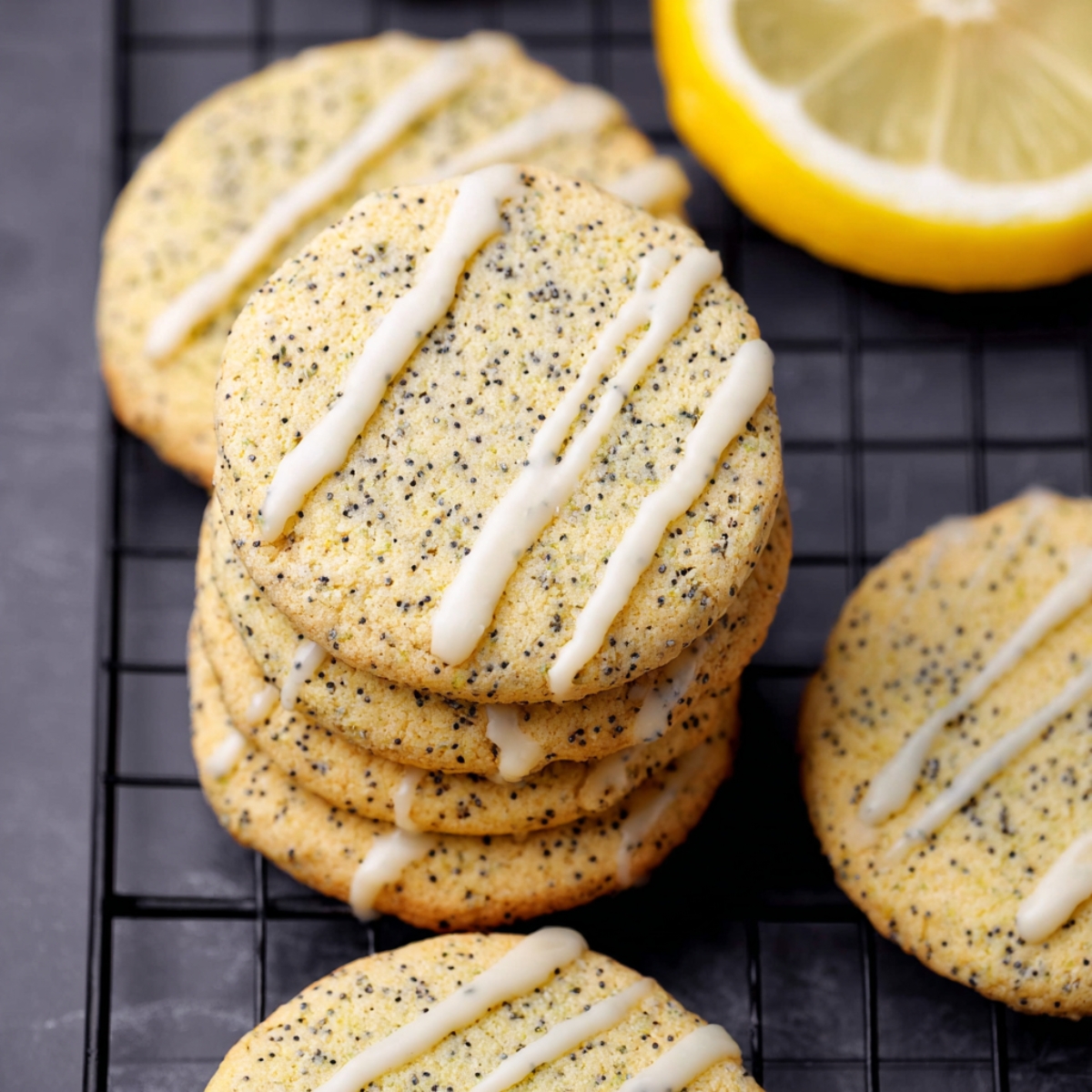 Golden lemon poppy seed cookies stacked neatly, drizzled with white glaze, with a fresh lemon slice in the background.
