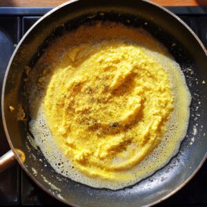 A pan with mashed paneer and potatoes being cooked, seasoned with pepper.