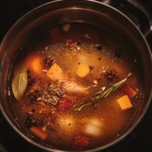 Pot of mulled-wine base gently simmering with orange chunks, bay leaf, rosemary, star anise, and spices.