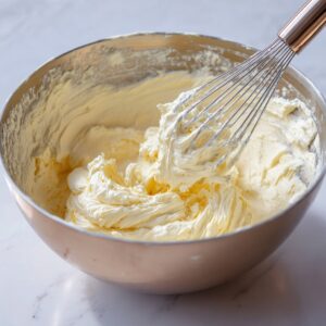 A large mixing bowl with fluffy whipped cream cheese mixture and a whisk.
