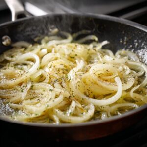 Delicious Parmesan Onion Squares Recipe 18 Onion slices cooking in a skillet with butter and seasonings, slowly softening and beginning to caramelize.