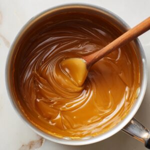 Close-up shot of thick golden caramel mixture being stirred quickly with a spoon in a saucepan, glossy texture, process shot