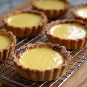 Freshly baked custard tarts cooling on a wire rack, with golden flaky crusts and smooth yellow custard filling.