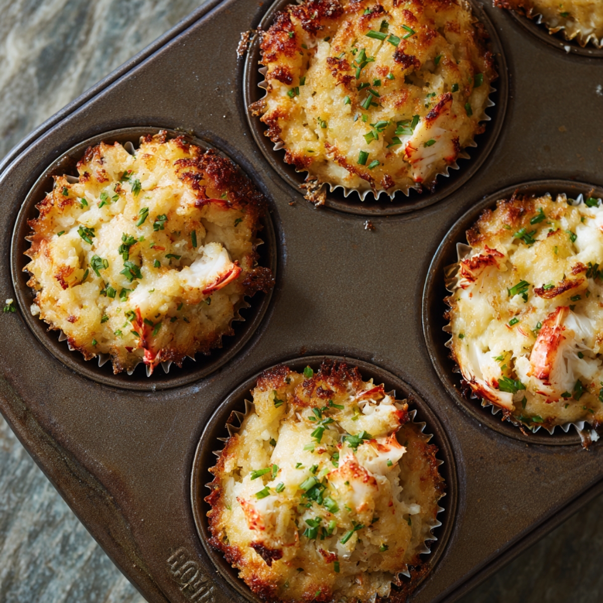 Baked crab cakes in a muffin tin, topped with fresh chopped parsley.