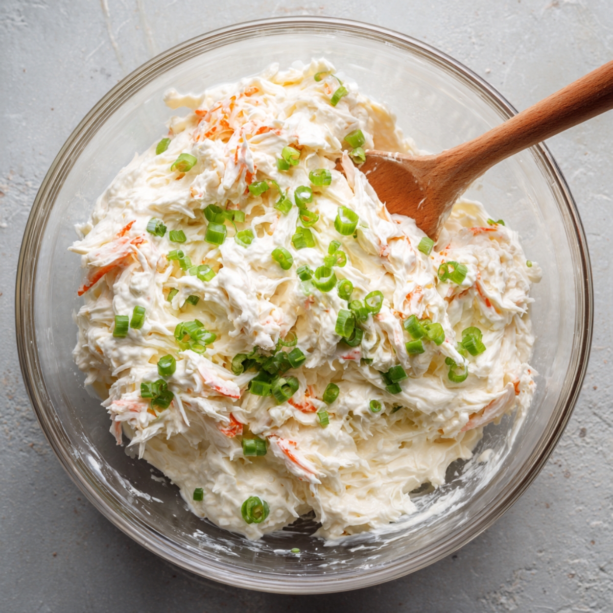 A bowl of creamy crab mixture with green onions, mixed with a wooden spoon.