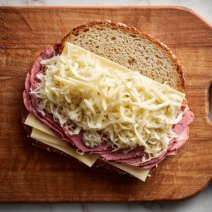 “Inside the sandwich: Russian dressing spread on bread, Swiss cheese as the base, thin corned beef slices, well-drained sauerkraut, and another layer of cheese before topping with the second slice.”