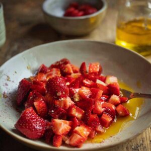 A bowl of diced strawberries mixed with maple syrup and a little liquid, with a fork resting in the bowl on a rustic wooden table.