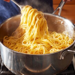 A large pot of spaghetti being tossed with tongs on the stove.