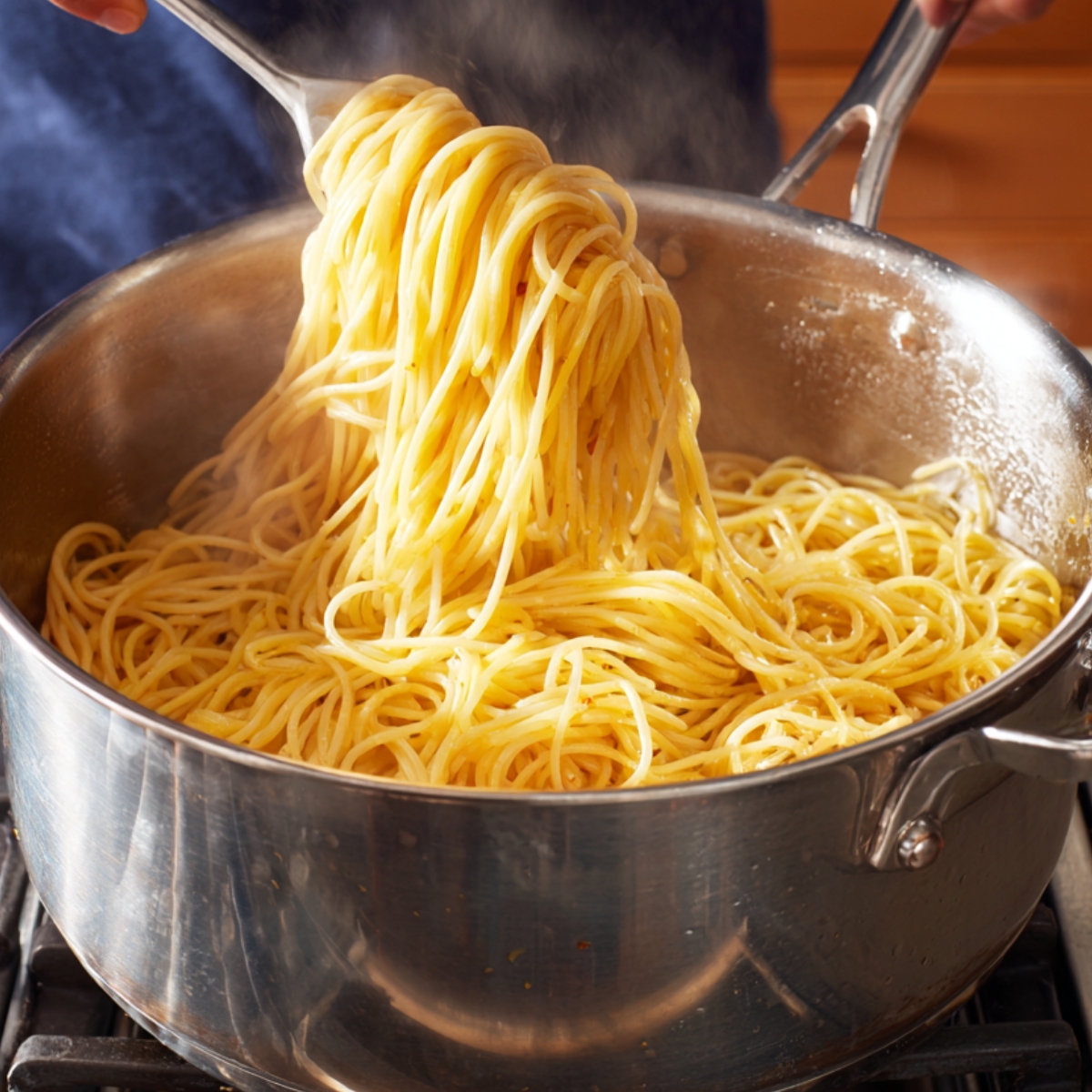 A large pot of spaghetti being tossed with tongs on the stove.