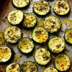 The Best Cheesy Garlic Zucchini Steaks Recips 19 Zucchini rounds seasoned with olive oil, herbs, and spices, arranged on a baking sheet ready for roasting.
