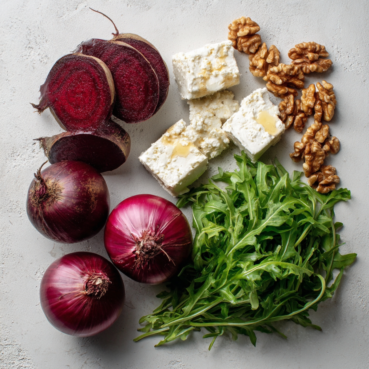 Fresh salad ingredients arranged on a light surface: sliced beets, red onions, arugula leaves, walnuts, and cubes of feta cheese drizzled with honey.
