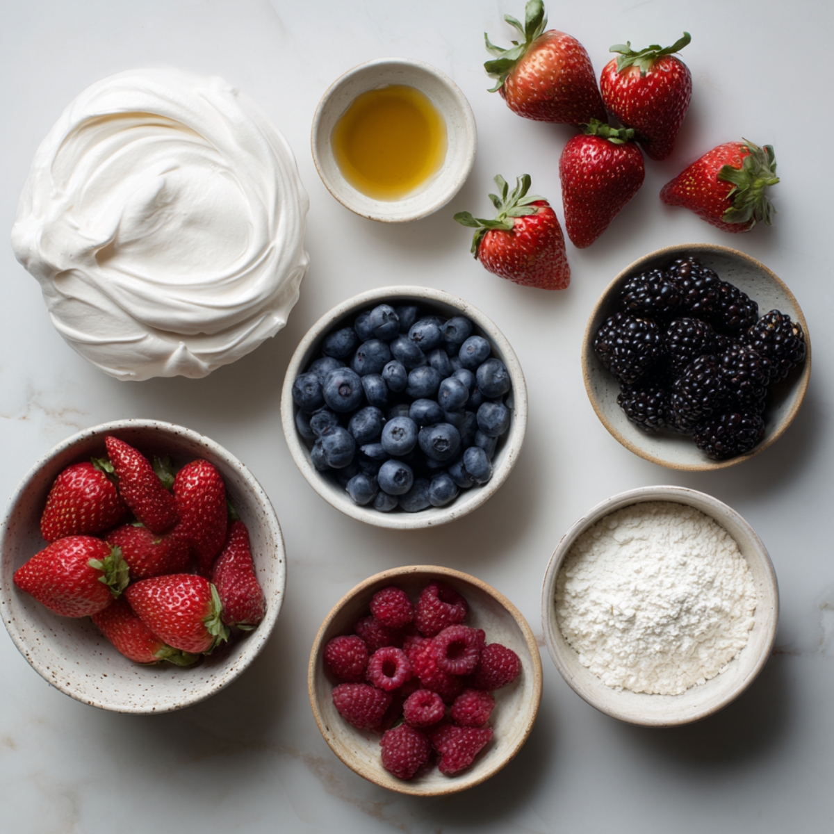 Ingrédients pour un dessert aux fruits : crème fouettée, miel, fraises, myrtilles, mûres, framboises, et sucre glace disposés dans des bols en céramique sur un plan de travail en marbre.