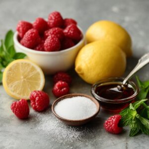 Fresh raspberry ingredients setup: bowl of raspberries, whole lemons, lemon half, sugar, honey, and mint leaves.