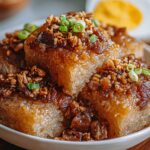 A plate of Biko Filipino Recipe cakes topped with golden latik, crunchy bits, and garnished with chopped green onions.
