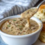 Bowl of Breakfast Gravy Recipe with biscuits – A bowl of hearty sausage gravy beside flaky golden biscuits on a rustic wooden table.