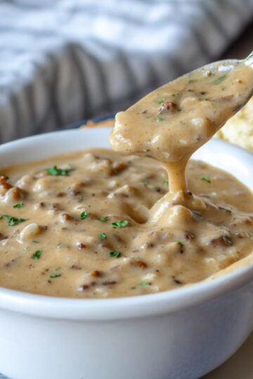 Bowl of Breakfast Gravy Recipe with biscuits – A bowl of hearty sausage gravy beside flaky golden biscuits on a rustic wooden table.
