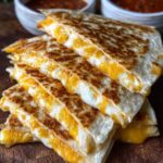 Sliced Cheese Quesadilla Recipe stacked on a plate, golden and cheesy, served with a bowl of red dipping sauce topped with herbs.