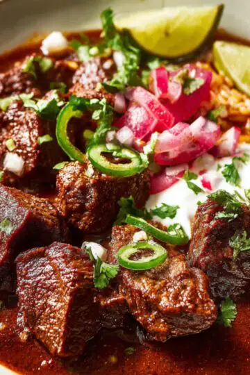 Final Serving Dish: Chili Colorado Recipe with tender beef in red sauce, garnished with pickled radishes, sour cream, jalapeño slices, and Mexican rice.